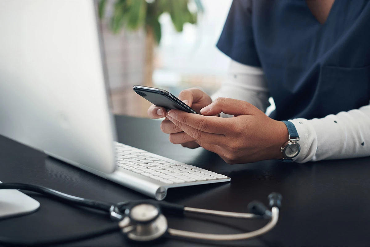 Nurse uses mobile phone at desk in front of computer